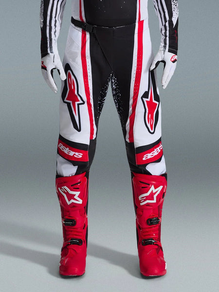 Alpinestars 2026 Techstar Nomur Pants, Motocross Pants, Black White and Red, worn with matching red boots and white gloves, featuring bold red logos on the thighs and 'astars' branding on the knees, multi-panel racing design for off-road performance