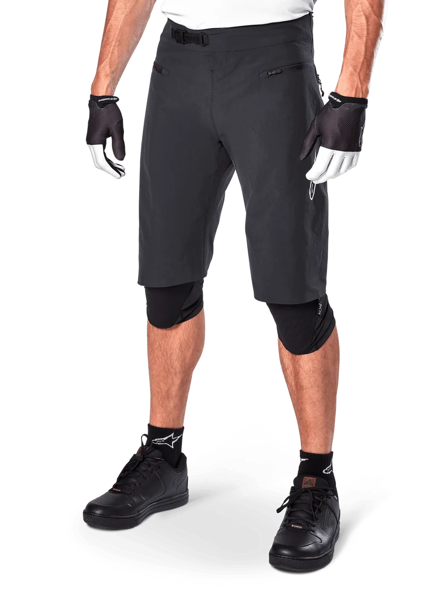 Alpinestars A-Aria Shorts, Mountain Biking Shorts, Black, knee-length with front zippered pockets and adjustable ratchet waist buckle, worn with black knee pads, socks, and cycling gloves