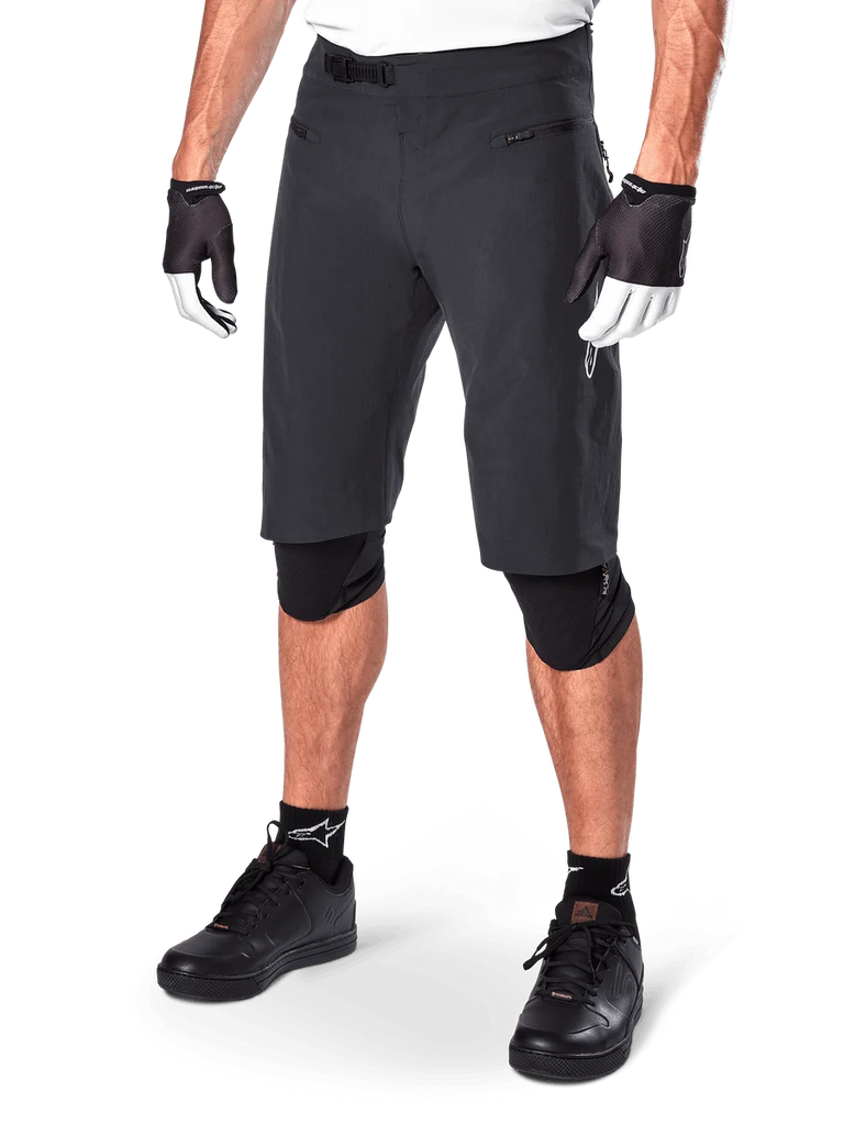 Alpinestars A-Aria Shorts, Mountain Biking Shorts, Black, knee-length with front zippered pockets and adjustable ratchet waist buckle, worn with black knee pads, socks, and cycling gloves