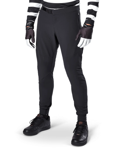 Alpinestars A-Aria Elite Pants, Black Mountain Bike Pants, featuring laser-cut ventilation on thighs and magnetic buckle closure, worn with black and white striped jersey and gloves, performance MTB gear for off-road cycling