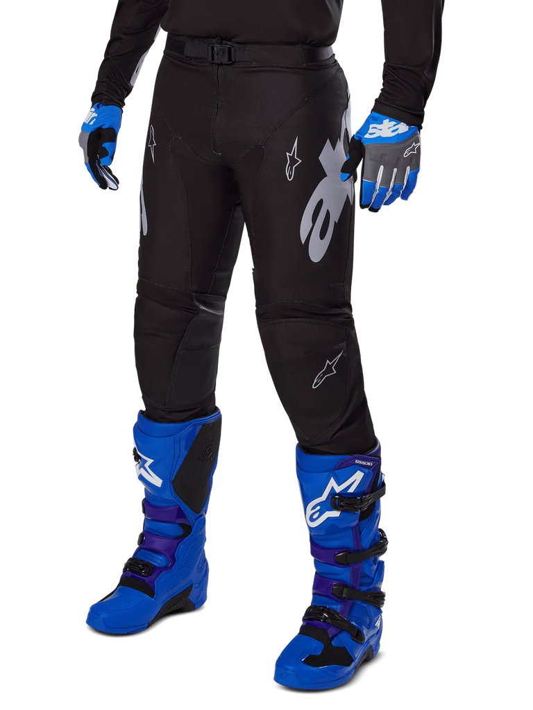 Alpinestars 2025 Racer Graphite Pants, Black Motocross Pants with white and gray graphics, worn with bright blue motocross boots and matching blue gloves, durable performance fabric for off-road riding