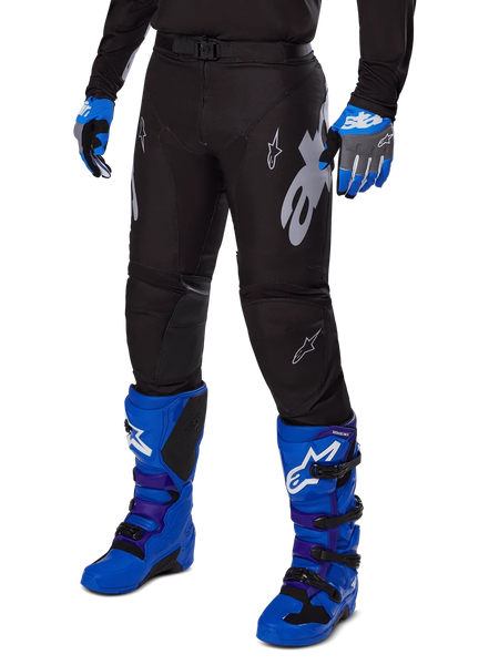 Alpinestars 2025 Racer Graphite Pants, Black Motocross Pants with white and gray graphics, worn with bright blue motocross boots and matching blue gloves, durable performance fabric for off-road riding