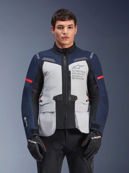 Alpinestars ST-7 2L GORE-TEX Jacket, Motorcycle Adventure Touring Jacket, Ice Gray and Dark Blue with Red accents, Waterproof and breathable, worn by a model with black gloves, featuring Alpinestars Exploration Equipment branding on the chest
