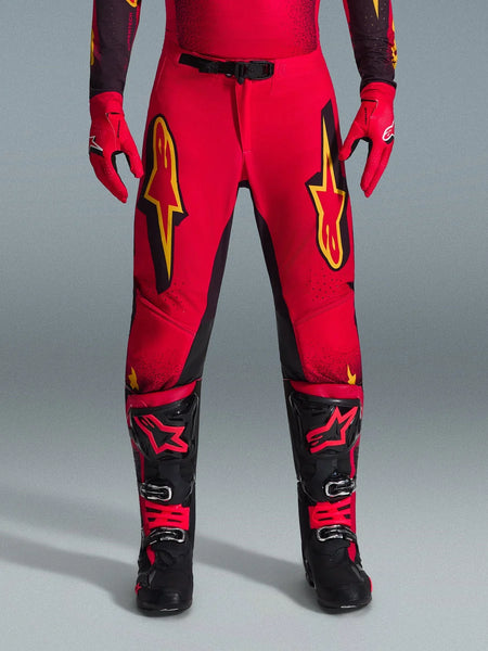 Alpinestars 2026 Supertech Scenz Pants, Motocross Pants, Red Black and Yellow, pro-level athletic fit with large yellow star logos on the thighs, paired with matching red gloves and black and red technical boots, designed for elite off-road racing performance