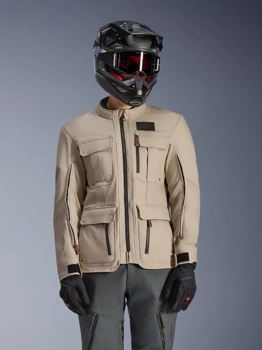 Alpinestars Borrego Drystar® Jacket, Adventure Motorcycle Jacket, Warm Gray, featuring multiple front cargo pockets and black zippers, worn with a black helmet, goggles, and dark gray riding pants, rugged textile design for touring