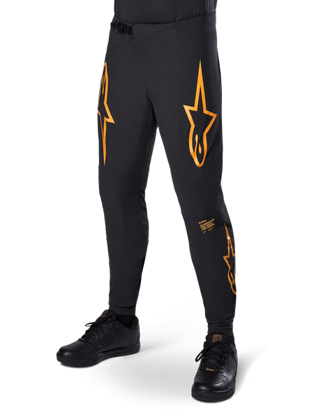 Alpinestars A-Supra Race Pants, Black with orange star graphics, MTB racing pants featuring laser-perforated ventilation and ratchet waist closure, slim performance fit for off-road cycling