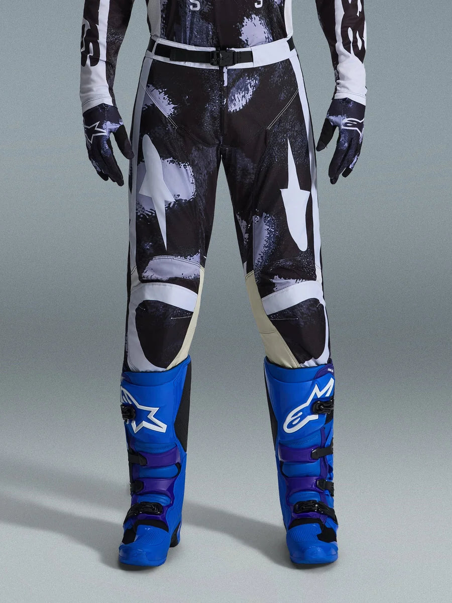 Alpinestars 2026 Racer Lahnd Pants, Motocross Pants, Iron Camo, worn with matching camouflage gloves and bright blue and purple boots, featuring stylized white star graphics on a dark camo pattern, technical magnetic buckle closure, professional off-road racing gear.