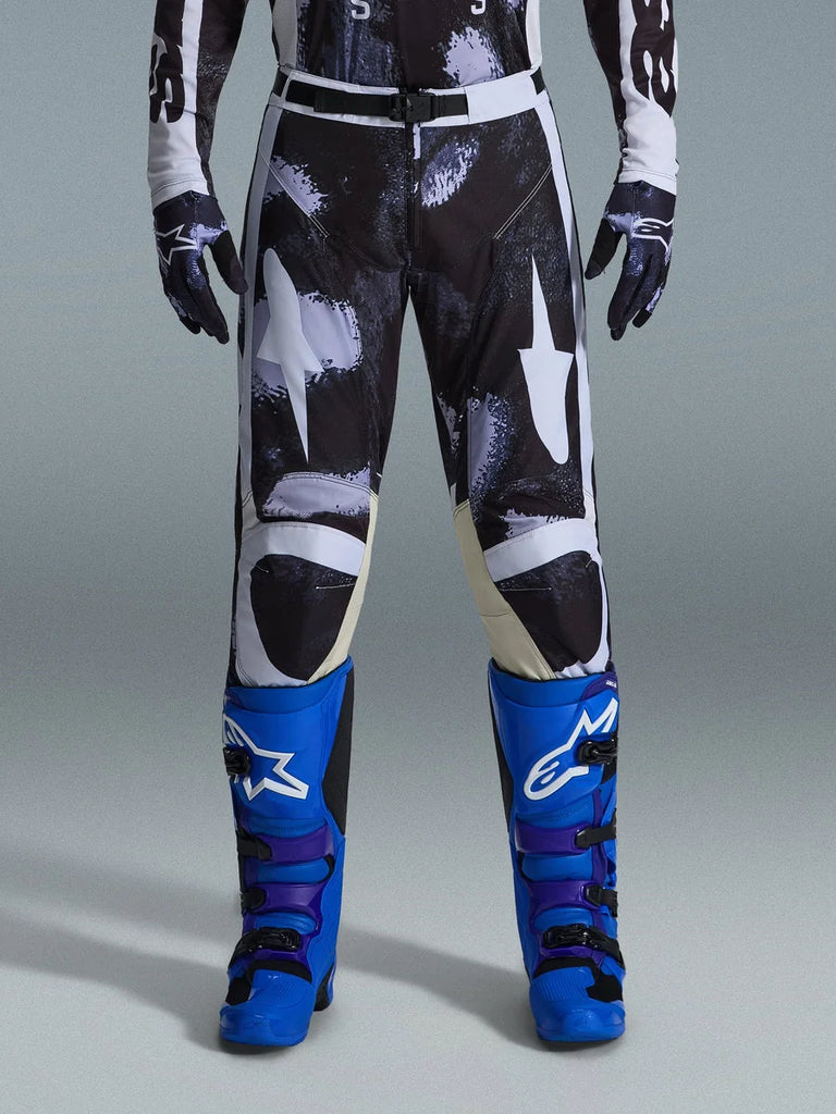Alpinestars 2026 Racer Lahnd Pants, Motocross Pants, Iron Camo, worn with matching camouflage gloves and bright blue and purple boots, featuring stylized white star graphics on a dark camo pattern, technical magnetic buckle closure, professional off-road racing gear.
