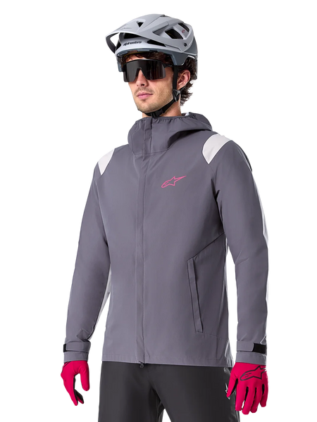 Alpinestars A-Dura Rain Jacket, Mountain Bike Rain Jacket, Dark Titanium Gray with pink logo and white shoulder accents, hooded design with front pockets, worn with pink gloves and a light gray cycling helmet