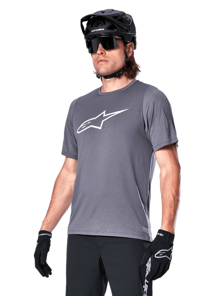 Alpinestars A-Dura Dri Astar Short Sleeve Jersey, Dark Gray, white chest logo and mesh sleeve panels, worn with black MTB helmet, sunglasses, and gloves, performance mountain biking apparel