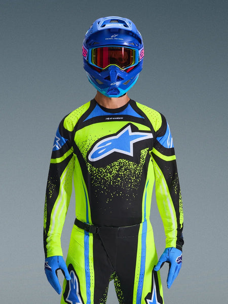 Motocross rider wearing the Alpinestars 2026 Techstar Nomur Jersey in Dark Navy and Yellow Fluo with blue accents, featuring a large blue logo on the chest, matching blue helmet and goggles, coordinated racing gear for off-road competition