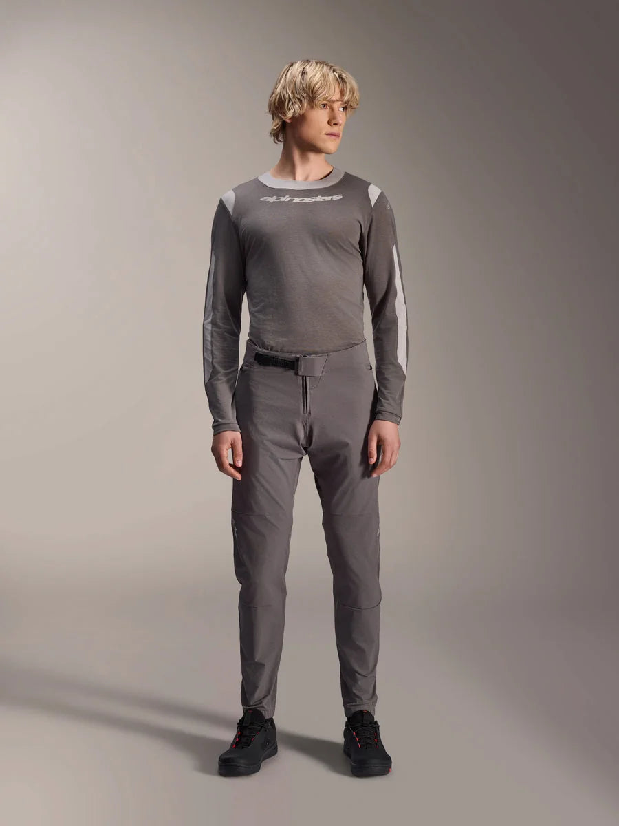Alpinestars A-Dura Elite Pants, Dark Gray mountain bike pants, full-body view, worn with a coordinating gray long-sleeve performance jersey featuring the Alpinestars logo, black shoes with red accents, athletic cycling outfit
