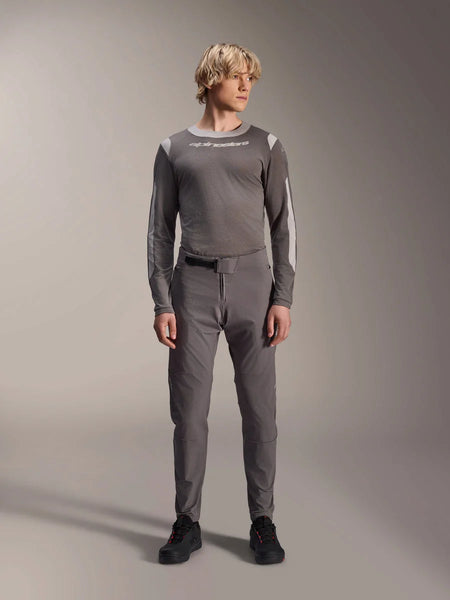 Alpinestars A-Dura Elite Pants, Dark Gray mountain bike pants, full-body view, worn with a coordinating gray long-sleeve performance jersey featuring the Alpinestars logo, black shoes with red accents, athletic cycling outfit