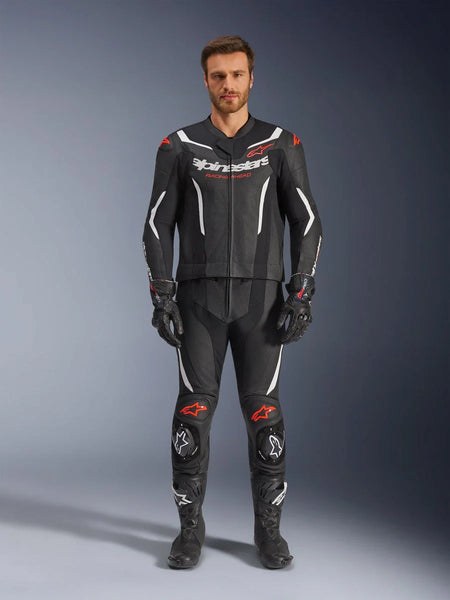 Alpinestars GP Force V2 2-Piece Leather Suit, Motorcycle Racing Suit, Black White and Red Fluo, worn by a model with matching black gloves and boots, featuring perforated leather panels, white and red fluo accents, and a sleek aerodynamic design for track and sport riding