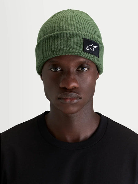 Alpinestars Unload Rib Cuff Beanie, sportswear knit winter hat, green, worn by a model showcasing the shallow-fit silhouette and SAstars woven front patch
