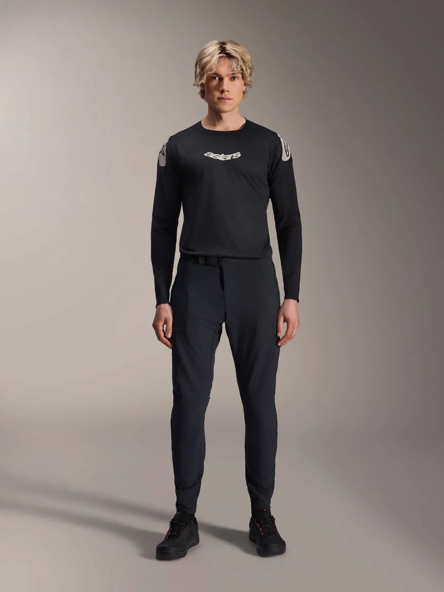Alpinestars A-Aria Elite Pants, Black Titanium MTB Pants, worn by a male model with a matching black long-sleeve jersey and sneakers, slim-fit performance design with magnetic buckle closure, technical mountain bike apparel