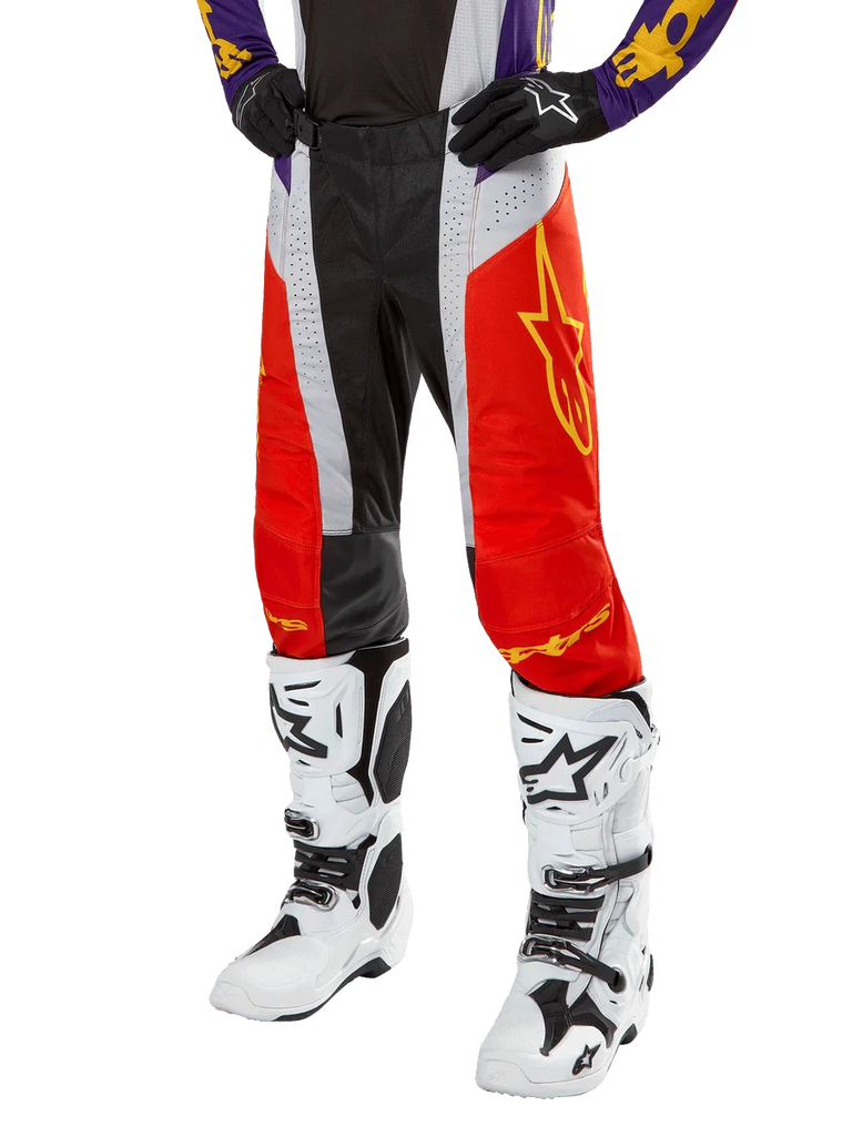 Alpinestars 2024 Techstar Ocuri Pants, Motocross Racing Pants, Hot Orange, Black, and White with Yellow Star Graphic, worn with purple jersey and white boots, durable performance gear for off-road competition