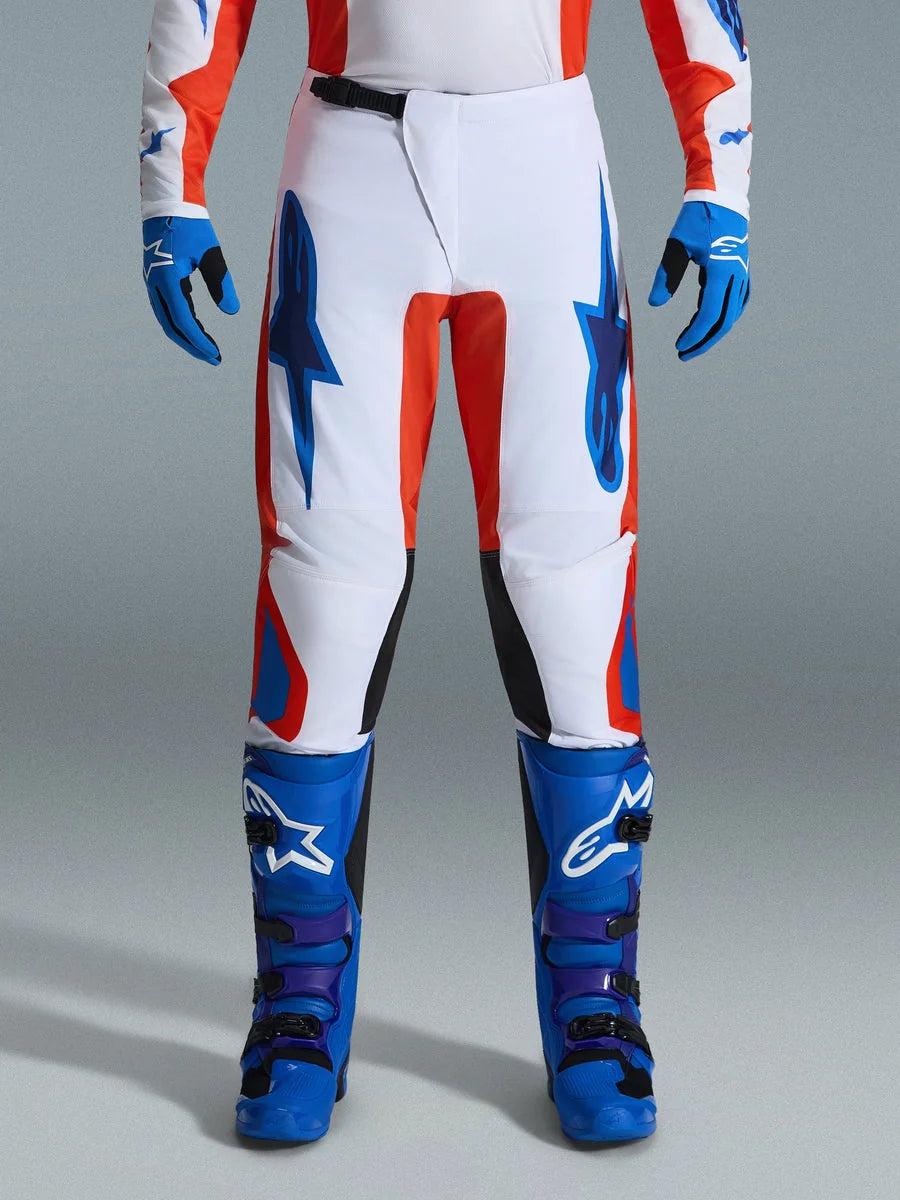 Alpinestars 2026 Fluid Grid Pants, Motocross Pants, Orange and UCLA Blue, worn with matching blue boots and gloves, featuring white chassis with bold blue logos and orange accents, ergonomic design for off-road performance