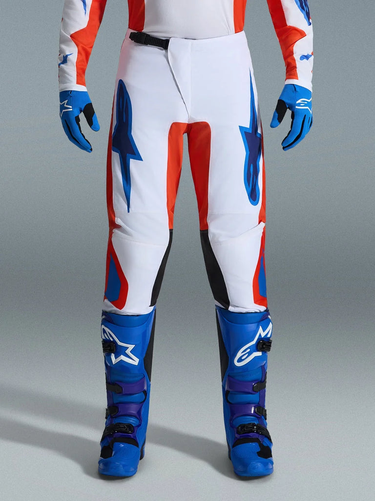 Alpinestars 2026 Fluid Grid Pants, Motocross Pants, Orange and UCLA Blue, worn with matching blue boots and gloves, featuring white chassis with bold blue logos and orange accents, ergonomic design for off-road performance