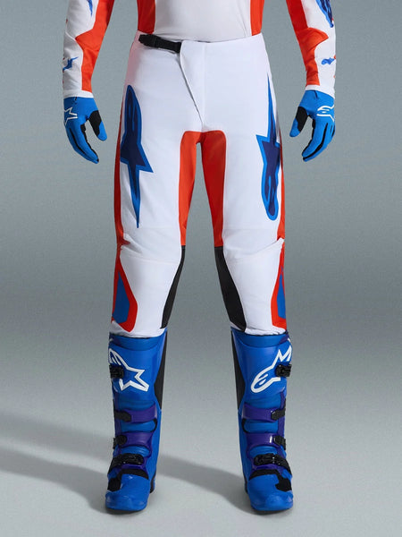 Alpinestars 2026 Fluid Grid Pants, Motocross Pants, Orange and UCLA Blue, worn with matching blue boots and gloves, featuring white chassis with bold blue logos and orange accents, ergonomic design for off-road performance