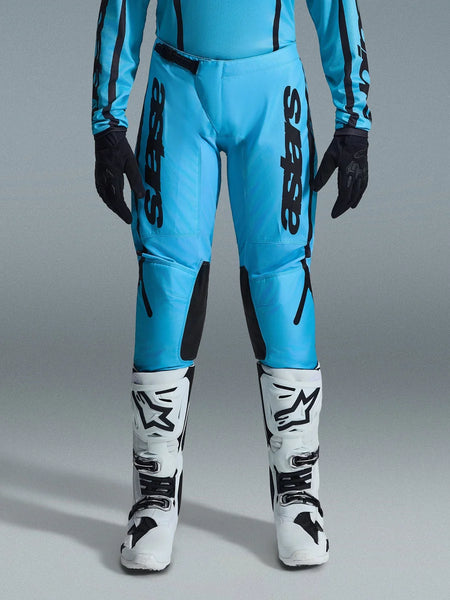 Alpinestars 2026 Woman Stella Fluid Apex Pants, Motocross Pants, Bright Cyan and Black, vertical black branding on thighs, black reinforced inner knee panels, shown with white and black motocross boots and black gloves, professional off-road gear for women