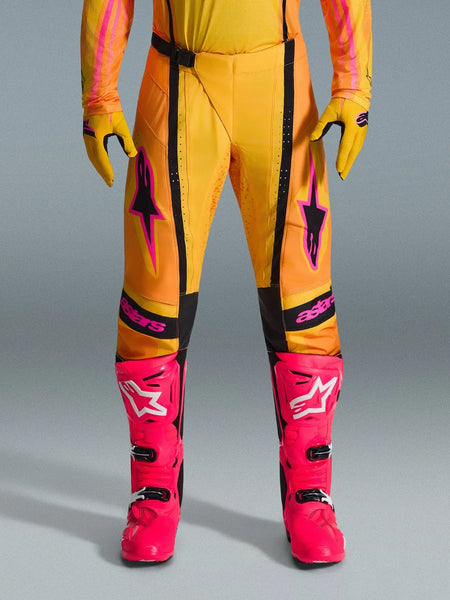 Alpinestars 2026 Techstar Nomur Pants, Motocross Pants, Orange Yellow and Pink, worn with matching yellow gloves and bright pink racing boots, featuring black panels and bold pink Alpinestars branding, technical off-road racing gear
