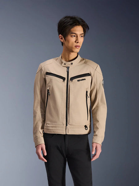 Alpinestars Bruiser Jacket, Beige motorcycle jacket worn by male model, featuring black zipper details on chest and side pockets, high snap collar, workwear-inspired urban riding wear, paired with black pants