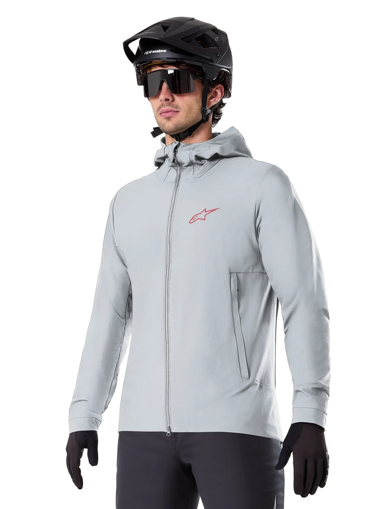 Alpinestars A-Dura Thermal Jacket, light gray insulated cycling jacket, hooded design with a small red logo, worn with a black helmet and gloves, technical mountain bike apparel for cold-weather riding