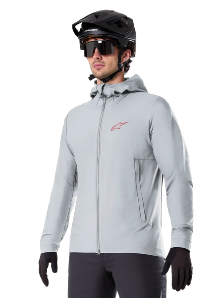 Alpinestars A-Dura Thermal Jacket, light gray insulated cycling jacket, hooded design with a small red logo, worn with a black helmet and gloves, technical mountain bike apparel for cold-weather riding