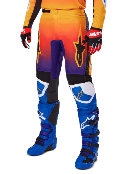 Alpinestars 2025 Fluid Wurx Pants, Motocross Pants, Multicolor orange red and purple gradient with black and blue panels, worn with blue boots and red gloves, featuring star logo graphics and white knee accents, durable performance gear for off-road racing