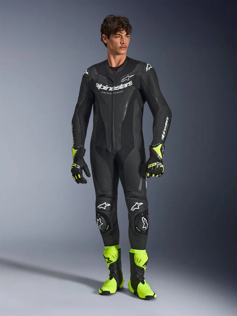 Alpinestars GP Force V2 Leather Suit, One-Piece Black Motorcycle Racing Suit, worn with fluorescent yellow boots and gloves, featuring white logos and perforated leather, sleek fitted design for track days