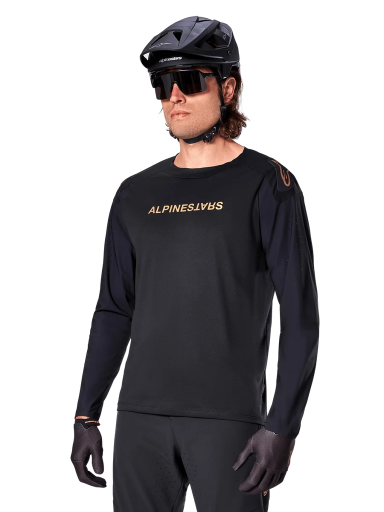 Alpinestars A-Aria Polartec Switch Long Sleeve Jersey, Black with gold logo, MTB mountain biking apparel, worn with a black helmet and sunglasses, featuring laser-cut ventilation on the sleeves and moisture-wicking Polartec fabric for off-road performance
