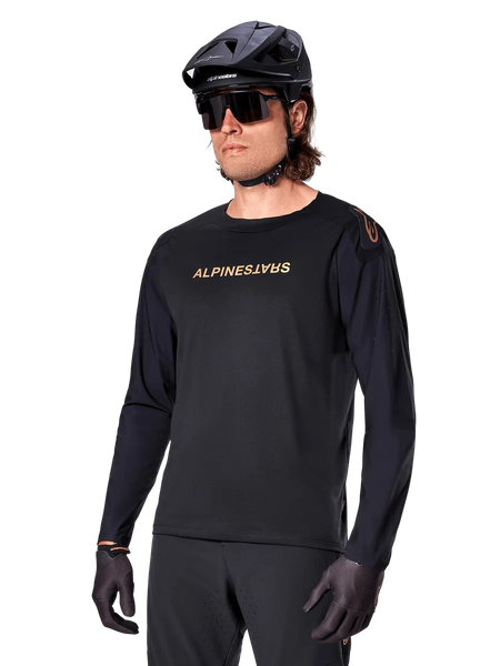 Alpinestars A-Aria Polartec Switch Long Sleeve Jersey, Black with gold logo, MTB mountain biking apparel, worn with a black helmet and sunglasses, featuring laser-cut ventilation on the sleeves and moisture-wicking Polartec fabric for off-road performance
