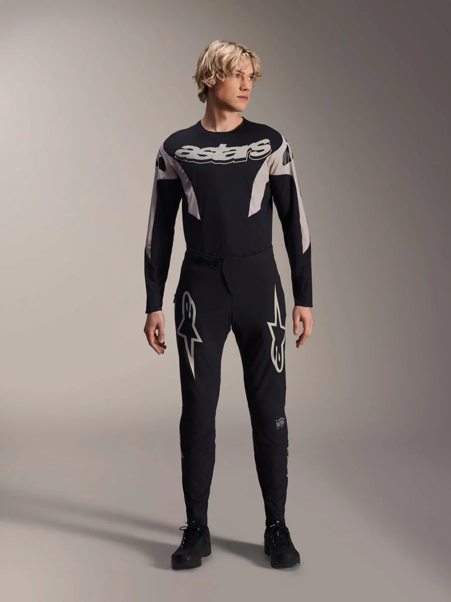 Alpinestars A-Supra Melt Pants and matching Long Sleeve Jersey, model wearing black MTB kit with large white star graphics on thighs and 'astars' branding on chest, professional mountain bike racing apparel.