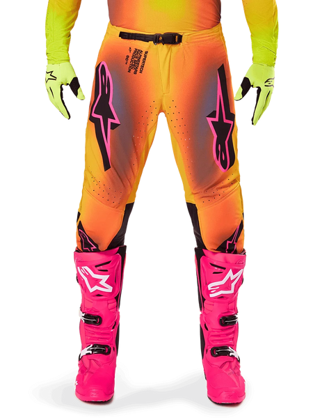 Alpinestars 2025 Supertech Lipan Pants, Motocross Pants, Orange and Yellow gradient with Pink and Black accents, worn with bright pink boots and neon yellow gloves, featuring laser-cut ventilation and a secure waist buckle, pro-level racing gear ensemble