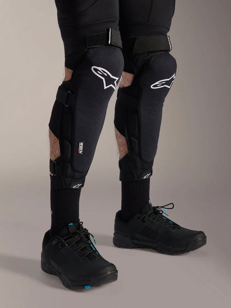 Alpinestars A-Impact Plasma Pro Knee Protectors, Black and White, featuring Nucleon PLASMA technology branding, worn with black socks and black mountain bike shoes, secure hook and loop straps, ergonomic protective gear for off-road cycling