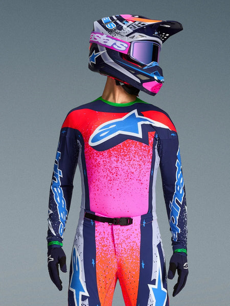 Motocross rider wearing the Alpinestars Limited Edition Supertech Records Jersey, vibrant pink and navy design with orange speckle patterns and a light blue star logo, matching helmet and goggles, professional racing gear.
