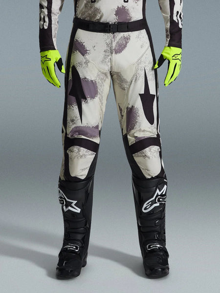 Alpinestars 2026 Racer Lahnd Pants, Motocross Pants, Sand Camo pattern with gray and purple abstract graphics, worn with neon yellow gloves and black boots, featuring black star logos on the thighs and a black waist belt, durable off-road racing gear