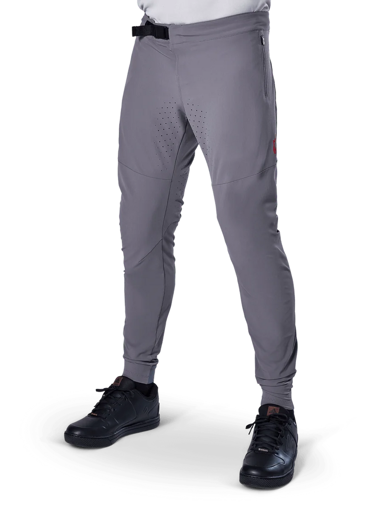 Alpinestars A-Aria Elite Pants, Dark Gray MTB Pants, laser perforated panels on thighs, black magnetic buckle closure, zippered pocket, red logo detail, slim performance fit, worn with black shoes
