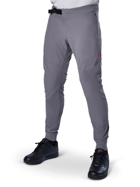 Alpinestars A-Aria Elite Pants, Dark Gray MTB Pants, laser perforated panels on thighs, black magnetic buckle closure, zippered pocket, red logo detail, slim performance fit, worn with black shoes