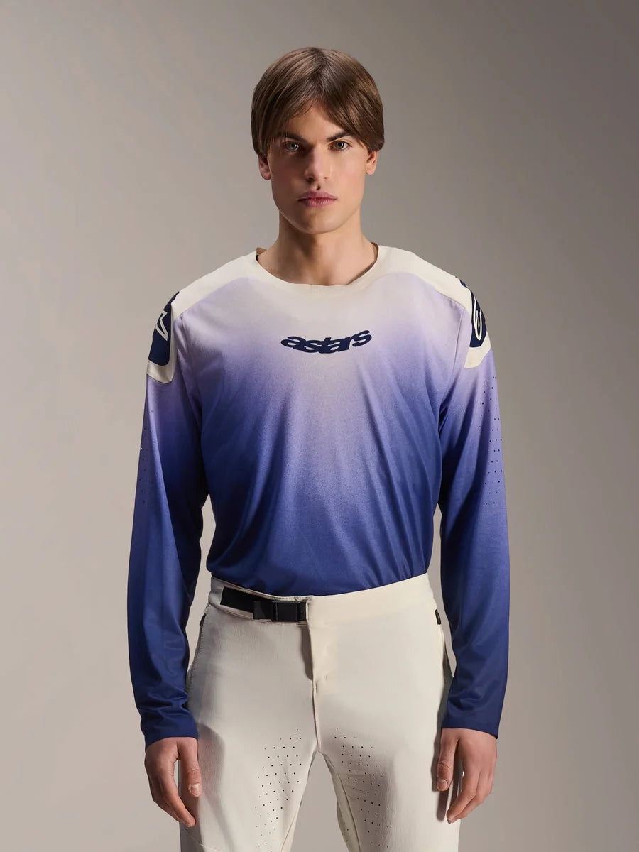 Alpinestars A-Aria Polartec Maker Elite Jersey, Long Sleeve MTB Jersey, Baja Blue with white-to-blue gradient, worn by a model with white pants, featuring dark blue chest logo and laser perforations on sleeves, performance mountain biking apparel