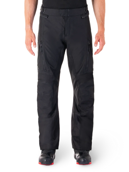 Alpinestars ST-1 Waterproof Pants, Black Motorcycle Touring Pants, front view featuring vertical zippered thigh pockets and adjustable waist tabs, worn with black red-soled boots, plain white background