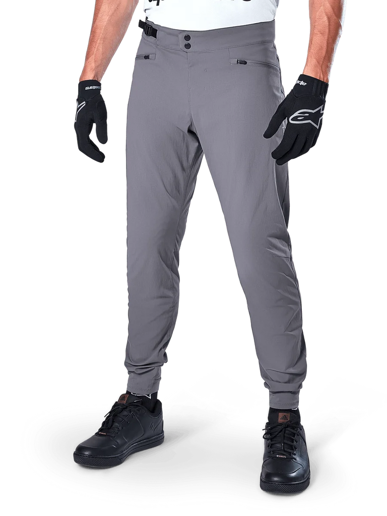 Alpinestars A-Dura Pants, Dark Gray MTB Pants, featuring double snap waist closure and zippered pockets, elasticated cuffs, worn with black cycling gloves and black sneakers