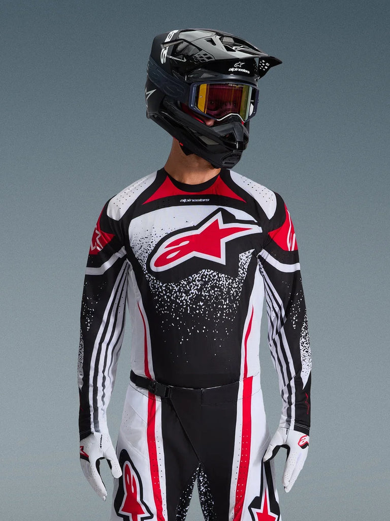 Alpinestars 2026 Techstar Nomur Jersey, Motocross Jersey, Black White and Red, worn by a rider with matching pants, black helmet, and white gloves, featuring a large red Astars logo and speckled graphic design, athletic race fit for off-road competition