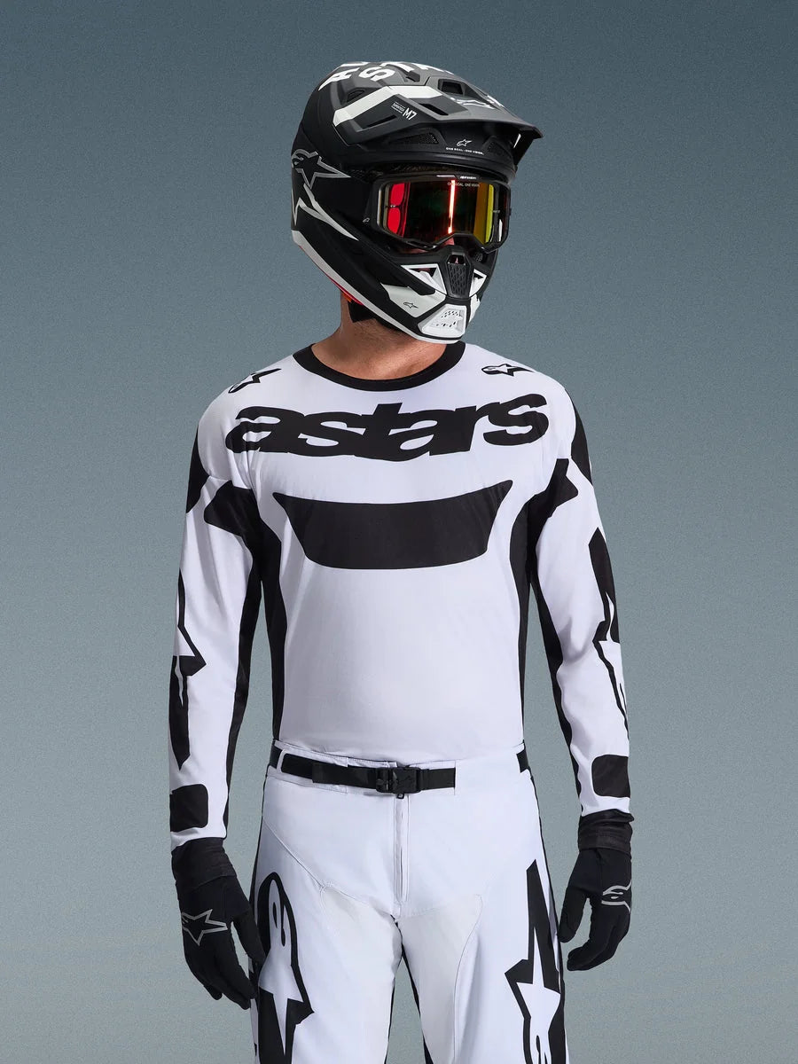 Motocross rider wearing the Alpinestars 2026 Racer Riway Jersey in White and Black, featuring 'astars' branding on the chest, paired with matching white and black pants, a black helmet with goggles, and black gloves, coordinated kit for off-road racing