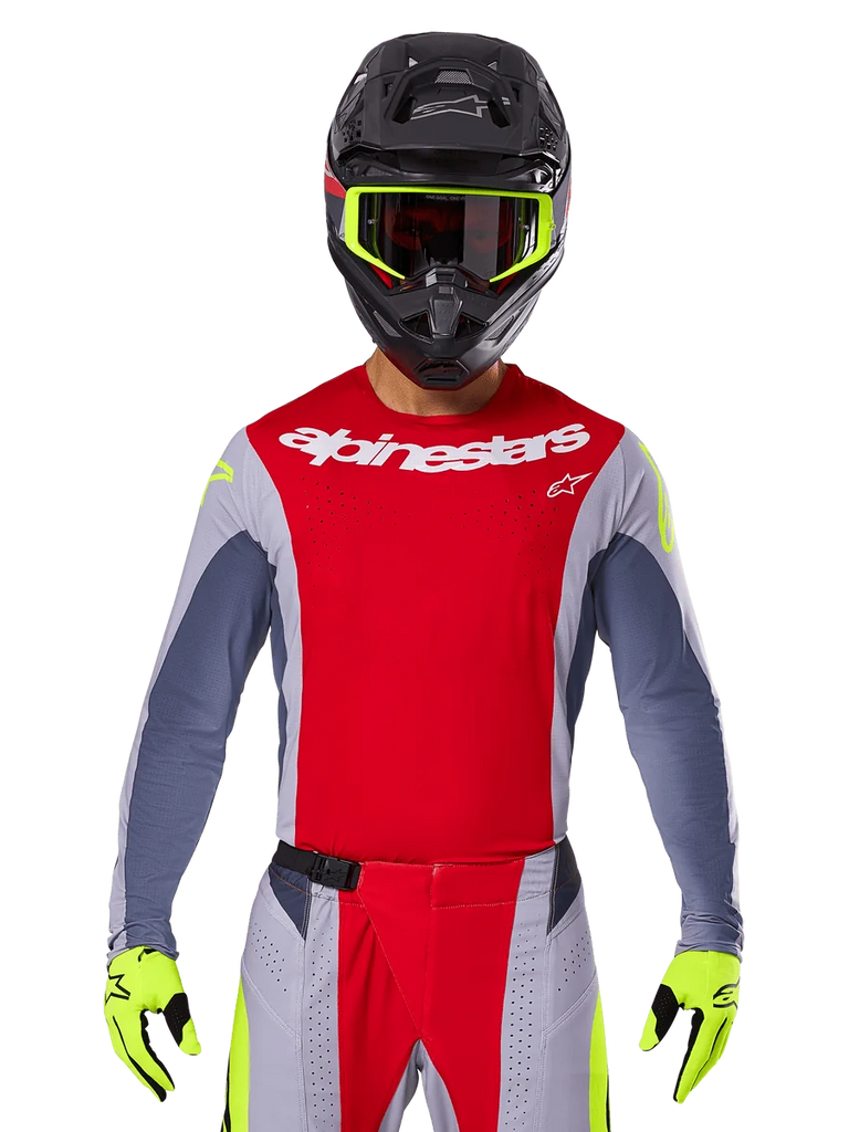Motocross rider wearing 2025 Techstar Melt Jersey and matching pants, Bright Red and Gray with white Alpinestars branding, black helmet with neon yellow goggles, matching neon yellow gloves, ventilated performance gear for off-road racing