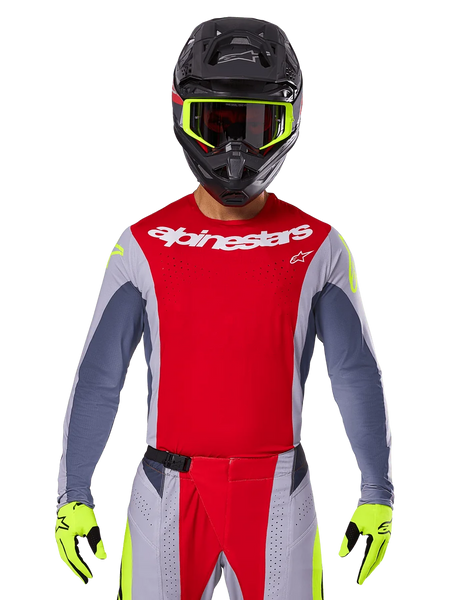 Motocross rider wearing 2025 Techstar Melt Jersey and matching pants, Bright Red and Gray with white Alpinestars branding, black helmet with neon yellow goggles, matching neon yellow gloves, ventilated performance gear for off-road racing