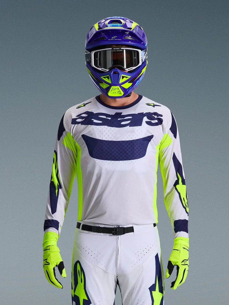 Alpinestars 2026 Racer Air Riway Jersey, Light Gray with Dark Blue astars logo, Fluo Yellow and Blue accents on sleeves, worn by a motocross rider with matching purple and neon yellow helmet and gloves, technical mesh fabric for off-road racing.