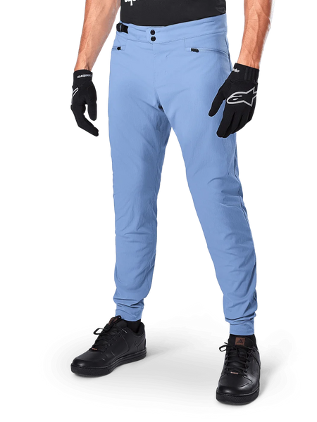 Alpinestars A-Dura Pants, Infinity Blue MTB Cycling Pants, featuring double snap front closure and zippered pockets, worn with black gloves and black shoes, durable 2-way stretch textile for off-road riding