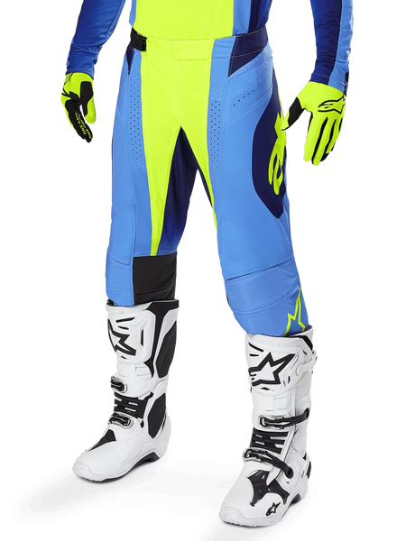 Alpinestars 2025 Techstar Melt Pants, Motocross Pants, Yellow Fluo Blue, worn with matching yellow and blue gloves and white motocross boots, featuring ergonomic cut and ventilation for off-road racing performance.